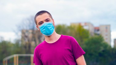 Arkaplanda pembe tişört ve mavi tıbbi maske takan yakışıklı, beyaz bir adam. Kopya alanı ile Coronavirus kavramı.