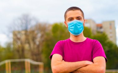 Arkaplanda pembe tişört ve mavi tıbbi maske takan yakışıklı, beyaz bir adam. Kopya alanı ile Coronavirus kavramı.