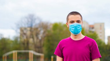 Arkaplanda pembe tişört ve mavi tıbbi maske takan yakışıklı, beyaz bir adam. Kopya alanı ile Coronavirus kavramı.