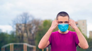 Arkaplanda pembe tişört ve mavi tıbbi maske takan yakışıklı, beyaz bir adam. Adam tıbbi maske takıyor. Kopya alanı ile Coronavirus kavramı.