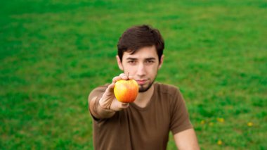 Fosforlu yakışıklı bir adam elinde bir elma tutuyor. Kopyalama alanı olan yeşil çimen.