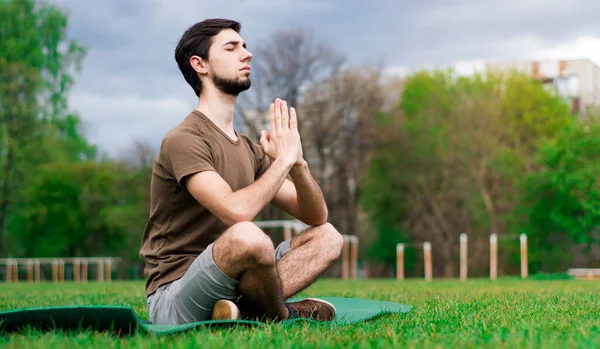 A handsome guy doing meditation on the grass of a stadium.