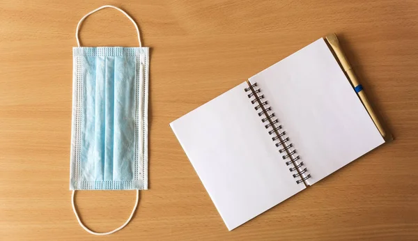 Ekolojik kalem ve mavi tıbbi maskeli defter ahşap bir arka planda yatıyor. Coronavirüs salgını konsepti.