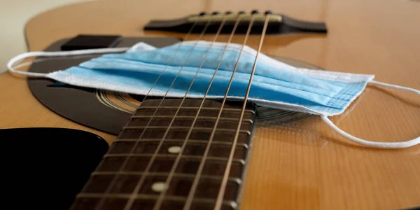 Mavi bir tıbbi maske akustik gitarın üzerinde yatar. Coronavirus müzik konsepti.