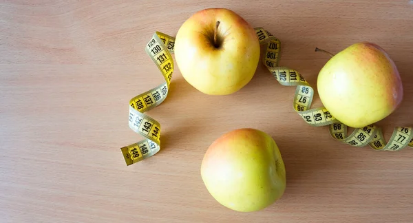 Strip for measurement and three apples lie on the wooden table.