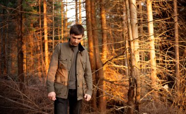 Genç esmer beyaz bir adam akşamleyin bir çam ormanının ortasında duruyor. Kopyalama alanı olan doğa kavramı.