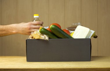 Adam gri bağış kutusuna bir şişe yağ koyuyor. Koronavirüs sırasında muhtaçlara ve açlıktan ölenlere bağışlar. Makarna, kraker, yağ, ekmek, salatalık, muz, domates, peynir.