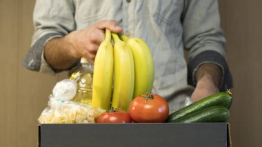 Bir adam bağış kutusuna muz koyar. Koronavirüs sırasında muhtaçlara ve açlıktan ölenlere bağışlar. Makarna, kraker, yağ, ekmek, salatalık, muz, domates.