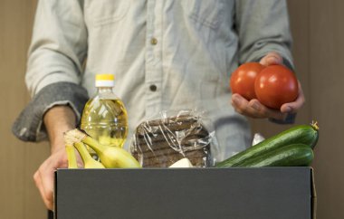 Adamın biri domatesleri bağış kutusuna koyuyor. Koronavirüs sırasında muhtaçlara ve açlıktan ölenlere bağışlar. Makarna, kraker, yağ, ekmek, salatalık, muz, domates, peynir.