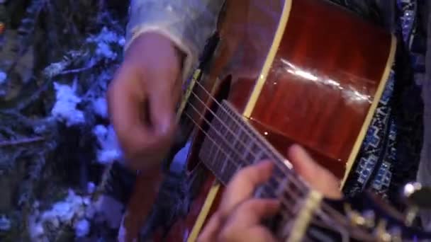 Un guitarrista de una chaqueta densa toca enérgicamente una púa sobre una guitarra acústica. — Vídeos de Stock