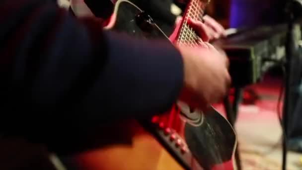 Κιθαρίστας που παίζει ενεργητικά μαύρη ακουστική κιθάρα με μπάντα στη σκηνή. — Αρχείο Βίντεο
