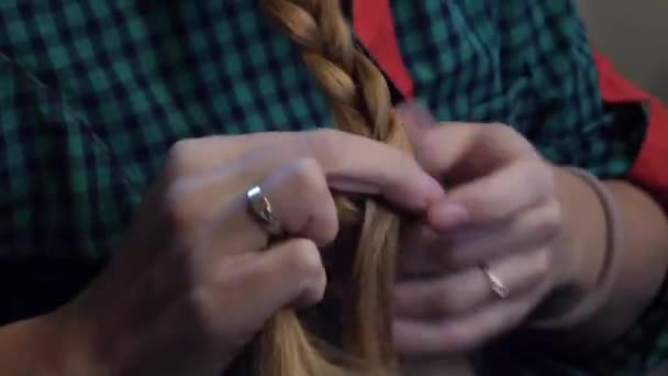 Caucasian woman in a green plaid shirt combing her hair in a braid — Stock Video