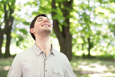 Güzel, genç bir esmer parkta dikiliyor, başını yukarı kaldırıyor ve gözlerini kapıyor ve gülümseyerek eğleniyor..