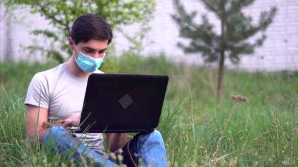 Ένας Νεαρός Άνδρας Ιατρική Μάσκα Κάθεται Στο Γρασίδι Κοντά Στο — Αρχείο Βίντεο
