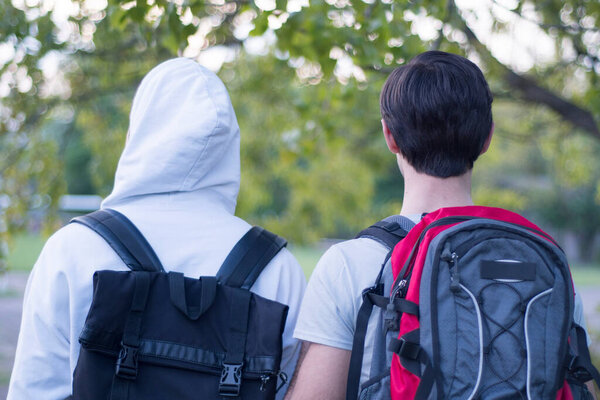 Two guys friends with tourist backpacks are walking in the forest. Back view