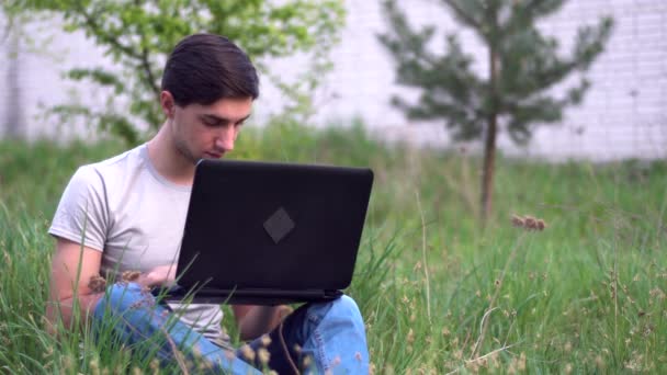 Ένας Νεαρός Καυκάσιος Κάθεται Στο Γρασίδι Κοντά Στο Σπίτι Και — Αρχείο Βίντεο