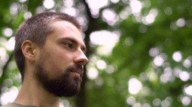 Parkta yakın planda gülümseyen sakallı beyaz bir adamın portresi. Kopya alanı ile ağaçların doğa arkaplanı.