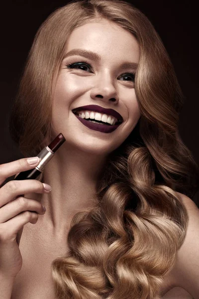 Beautiful blonde in a Hollywood manner with curls, dark lips, lipstick in hand. Beauty face and hair. — Stock Photo, Image