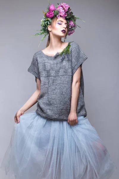Vacker flicka med blommor på hennes huvud i Modekläder poserar mot bakgrunden i studion. — Stockfoto