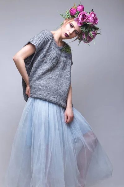 Gyönyörű lány virággal a fején pózol a háttérben a stúdióban divat ruhák. — Stock Fotó