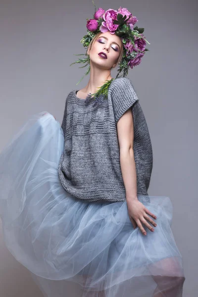 Bella ragazza con fiori sulla testa in abiti di moda in posa sullo sfondo in studio . — Foto Stock