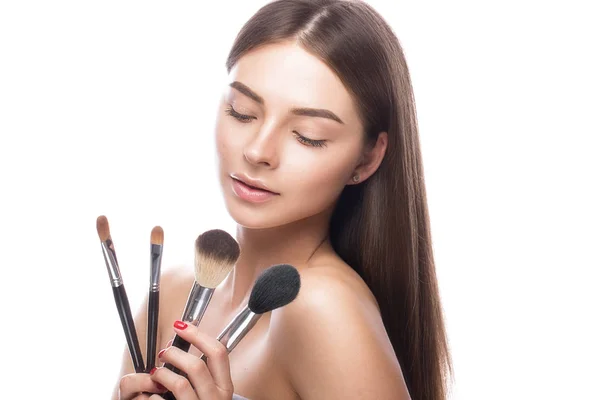 Hermosa joven con un maquillaje natural ligero, cepillos para cosméticos y piel perfecta. Cara de belleza . — Foto de Stock