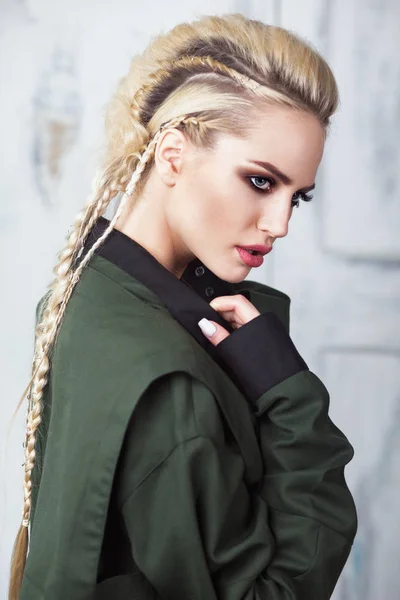 Creative unusual blond girl in designer clothes and braids on her head posing in the studio — Stock Photo, Image