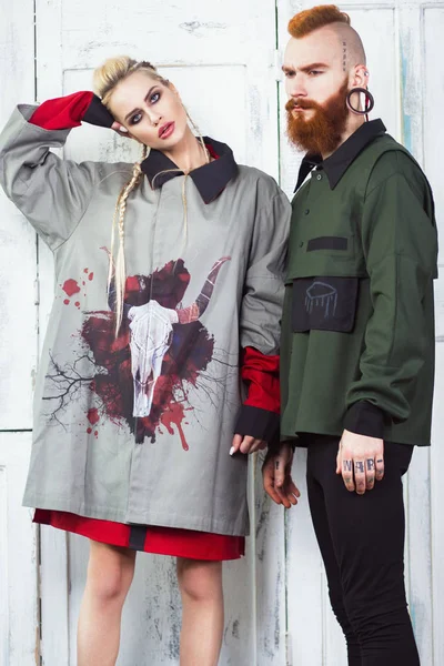 Creative unusual blond girl and red-haired man in designer clothes and braids on their heads.