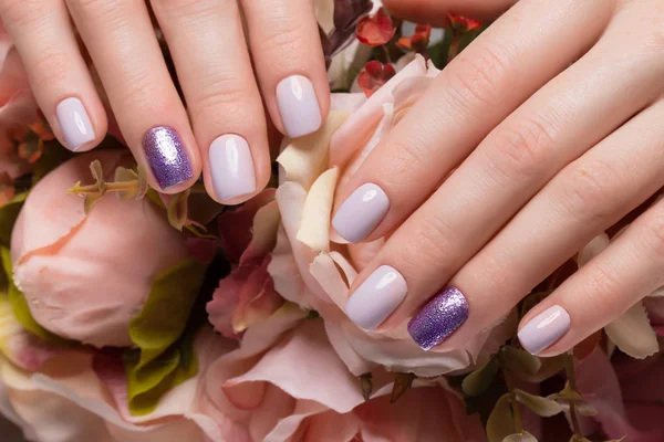 Manicure puro roxo em mãos femininas em fundo de flores. Desenho do prego — Fotografia de Stock