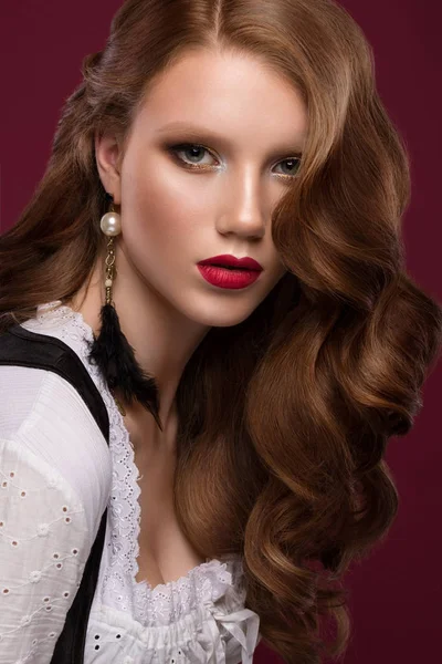 Beautiful redhair model: curls, bright gold makeup, jewelry and red lips. The beauty face.
