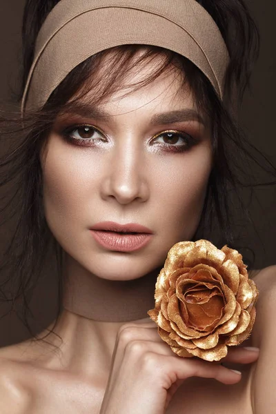 Schöne Frau mit hellem Make-up und perfekter Haut mit goldenen Blumen in der Hand. Schönheit Gesicht. — Stockfoto