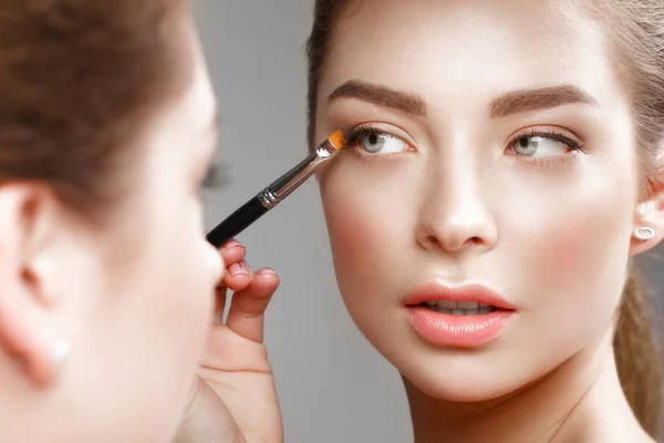 Gyönyörű lány a make-up teszi magát a tükörben. Szépség arc. — Stock Fotó