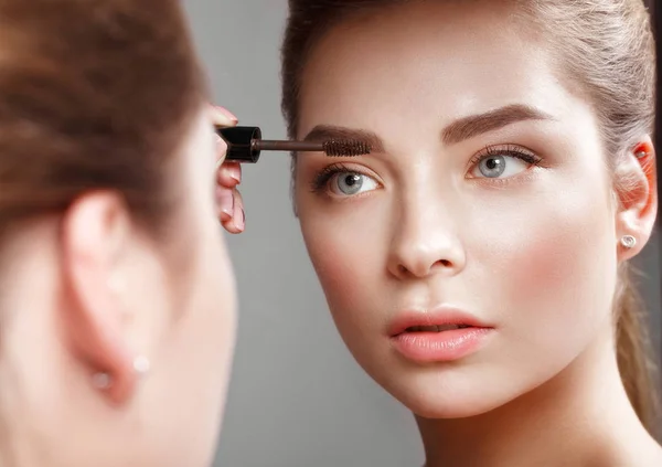 Mooi meisje maakt zelf een make-up in de spiegel. Schoonheid gezicht. — Stockfoto