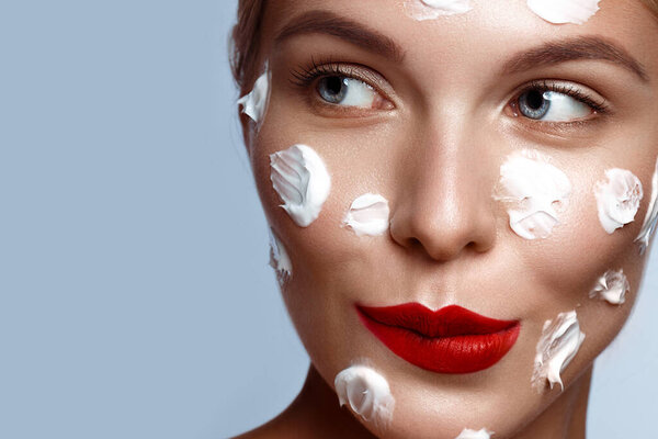 Beautiful fresh girl with cosmetic cream on the face, natural make-up and green leaves. Beauty face.