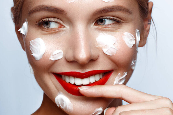 Beautiful fresh girl with cosmetic cream on the face, natural make-up and red lips. Beauty face.