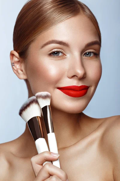 Gyönyörű lány piros ajkak és klasszikus smink kozmetikai kefék a kézben. Szépség arc. — Stock Fotó