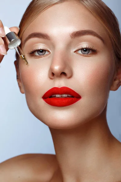 Mooi meisje met rode lippen en klassieke make-up met olie voor de huid in de hand. Schoonheidsgezicht. — Stockfoto