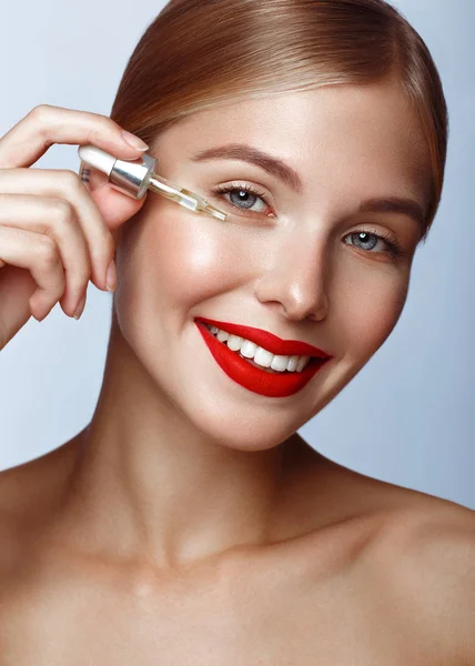 Beautiful girl with red lips and classic makeup with oil for skin in hand. Beauty face. — Stock Photo, Image