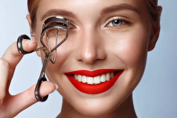 Vacker tjej med röda läppar och klassisk makeup med locktång i handen. Skönhetsansikte. — Stockfoto