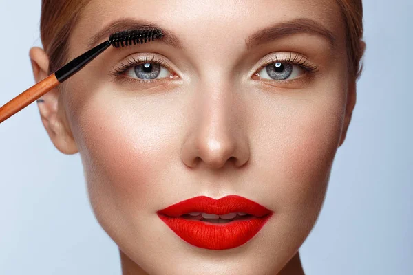 Beautiful girl with red lips and classic makeup with cosmetic brow brush in hand. Beauty face. — 스톡 사진