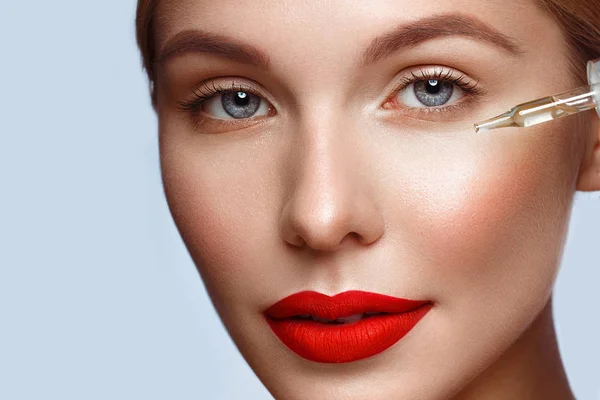 Hermosa chica con labios rojos y maquillaje clásico con aceite para la piel en la mano. Cara de belleza . — Foto de Stock