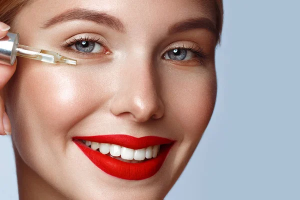 Schönes Mädchen mit roten Lippen und klassischem Make-up mit Öl für die Haut in der Hand. Schönheit Gesicht. — Stockfoto