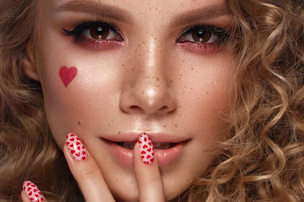 Pretty girl with curls hairstyle, classic makeup, freckles, nude lips and manicure design with hearts. Beauty face. The image for Valentines Day