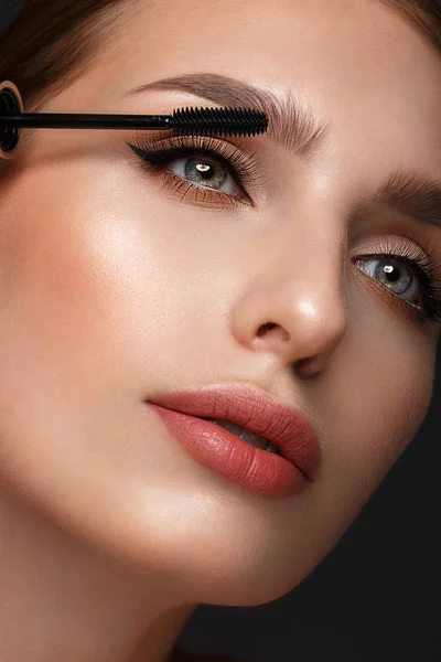Mooi meisje met sexy lippen en klassieke make-up met cosmetische mascara borstel in de hand. Schoonheidsgezicht. — Stockfoto