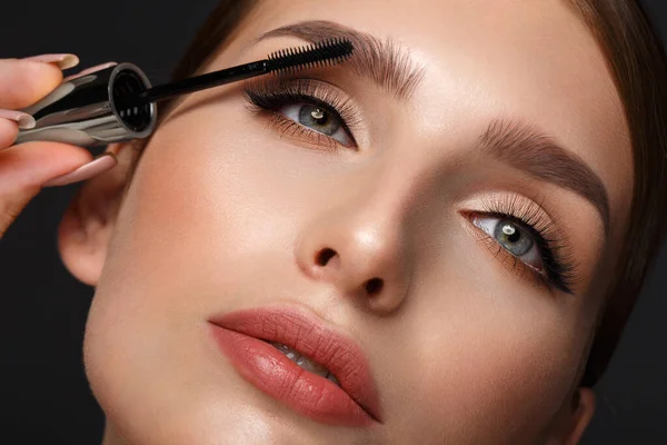 Mooi meisje met sexy lippen en klassieke make-up met cosmetische mascara borstel in de hand. Schoonheidsgezicht. — Stockfoto