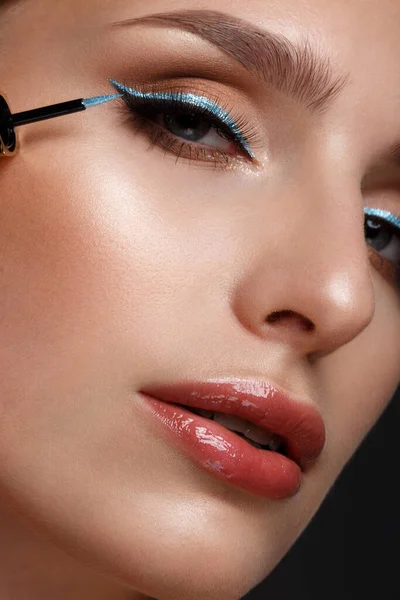 Menina bonita com lábios sexy e maquiagem clássica com delineador azul cosmético na mão. Cara de beleza . — Fotografia de Stock