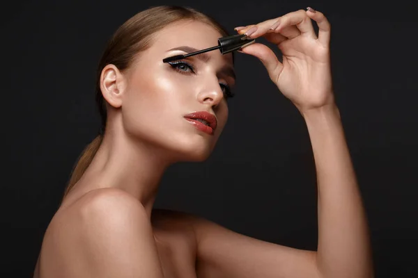 Mooi meisje met sexy lippen en klassieke make-up met cosmetische mascara borstel in de hand. Schoonheidsgezicht. — Stockfoto