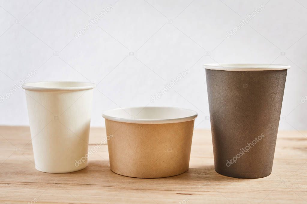 three different paper coffee cups on wooden background, close up