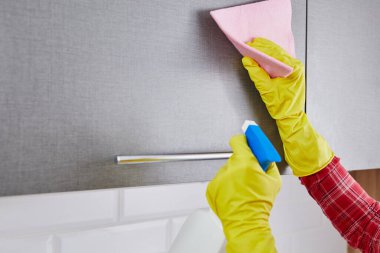 woman in protective gloves with spray cleaning kitchen cabinet