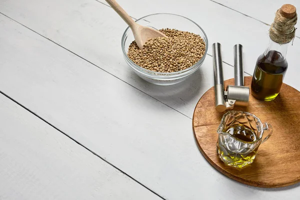 Hemp seed in a glass bowl and garlic pressing masher on the table, Cold pressed oil in a glass jar. — 图库照片